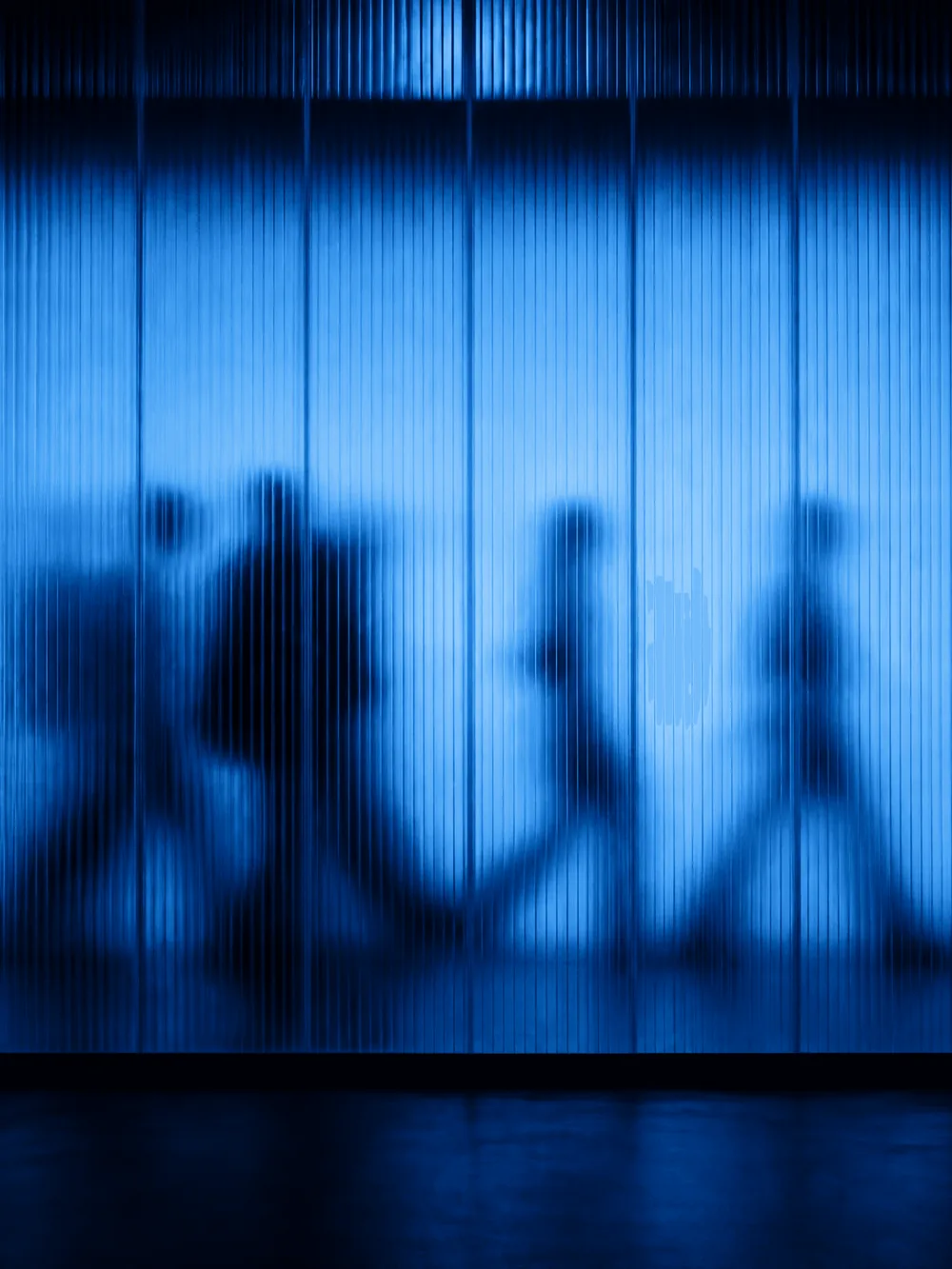Menschen gehen hinter einer Glaswand vorbei, nur als Schatten erkennbar